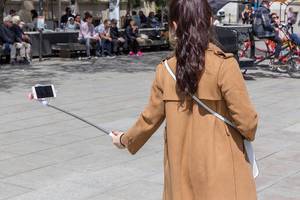 Woman takes a selfie with a selfiestick in front of the cathedral at the Placita de La Seu in Barcelona, Spain