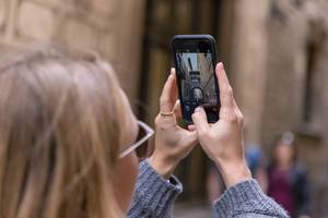 Woman taking a phone picture of the tourist attraction and mediterranean Skywalk "Pont Gòtic" in the Carrer del Bisbe Alley in Barcelona, Spain
