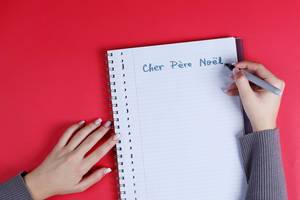 Woman writing Cher Pere Noel text on notebook, red background