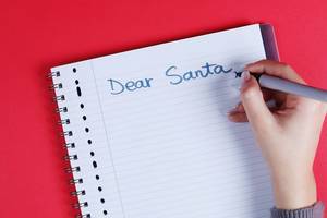 Woman writing Dear Santa text on notebook, red background, close-up