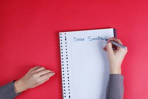 Woman writing Dear Santa text on notebook, red background