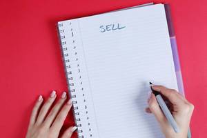 Woman writing Sell text on notebook, red background