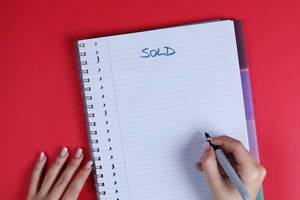 Woman writing Sold text on notebook, red background