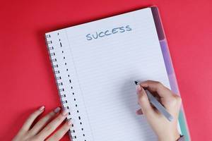 Woman writing Success text on notebook, red background