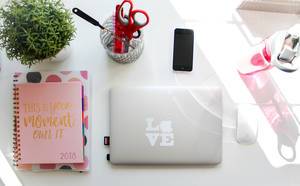 Womens desk at home with a bottle , macbook, notebooks and an iphone