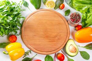 Wooden kitchen Board surrounded by vegetables and salad mix. Ingredients for cooking