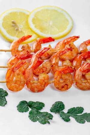 Wooden skewers with tails of grilled shrimp with lemon circles on a white plate