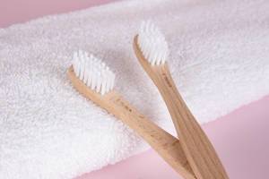 Wooden toothbrushes with towel on pink background