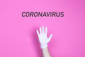 Wort Coronavirus über einer Hand mit medizinischem Handschuh vor pinkem Hintergrund