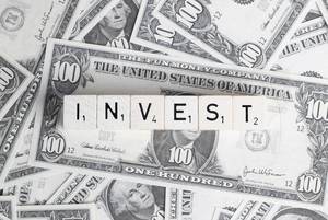 Würfel bilden das Wort INVEST (Investieren) auf verteilten Dollarnoten