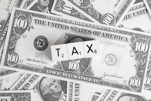 Würfel mit Buchstaben bilden das Wort TAX (Steuern) auf Hintergrund aus Dollarnoten