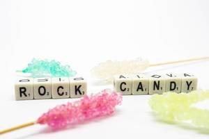 Würfel zeigen das Wort "Rock Candy" - Kandiszucker, umgeben von süßen Zuckerspießen, auf weißem Untergrund