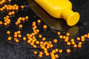Yellow plastic bottle and fresh sea buckthorn berries on black background. The concept of natural cosmetics
