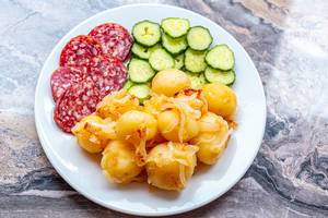 Young boiled potatoes with smoked sausage slices and cucumbers on a plate