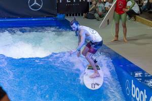 Young man riding the permanent wave of the surf machine Citywave at fair Boot Düsseldorf 2018
