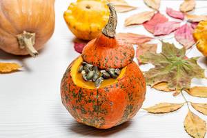 Yummy Halloween pumpkin with seeds on a white wooden background with autumn yellow leaves