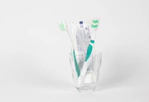Zahnbürsten und eine Tube Zahnpasta im Glas vor weißem Hintergrund