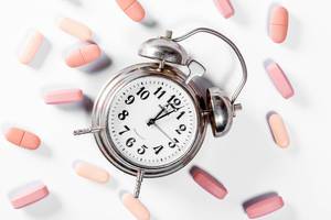 Zeit die Medikamente einzunehmen – Pillen verteilt um alten Wecker aus Metall vor weißem Hintergrund