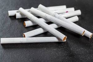 Zigaretten verstreut auf einem schwarzen Hintergrund als Symbolik für Gesundheitsschädlichkeit