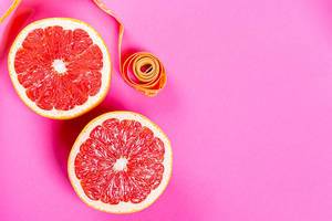 Zitrusfrüchte: Halbierte reife Grapefruit, auf rosa Hintergrund mit Maßband