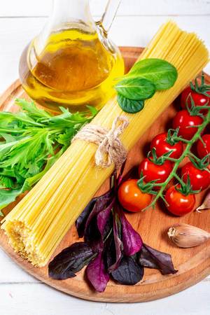 Zutaten, um Spaghetti zu kochen, auf einem runden Küchenbrettchen aus Holz mit Olivenöl in einer Glaskaraffe