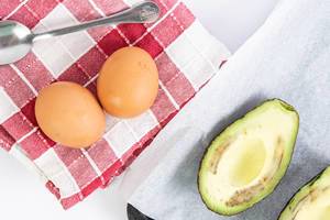 Zwei Eier liegen neben einer halbierte Avocadofrucht