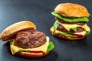 Zwei hausgemachte Burger mit Rindfleisch-Patties, Käse und Gemüse auf schwarzem Hintergrund