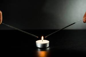 Zwei Wunderkerzen kurz vor der Flamme einer Kerze, vor grau-schwarzem Hintergrund